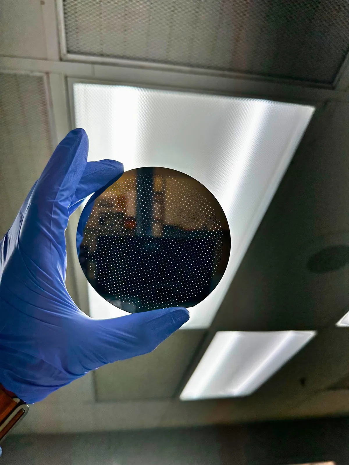 Gloved technician inspecting a patterned wafer under cleanroom lighting — Heisler Semiconductor