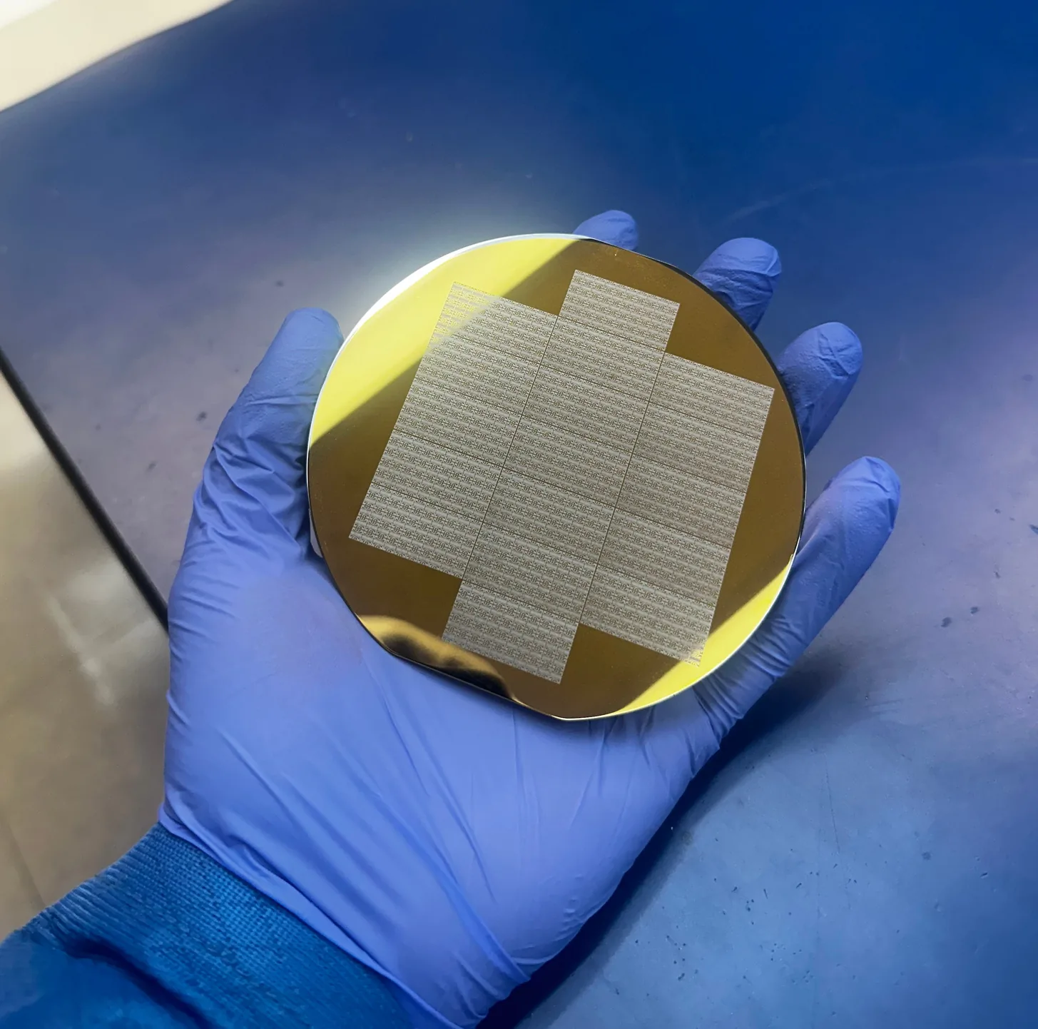 Gloved hand holding a gold-metallized wafer with a dense die array