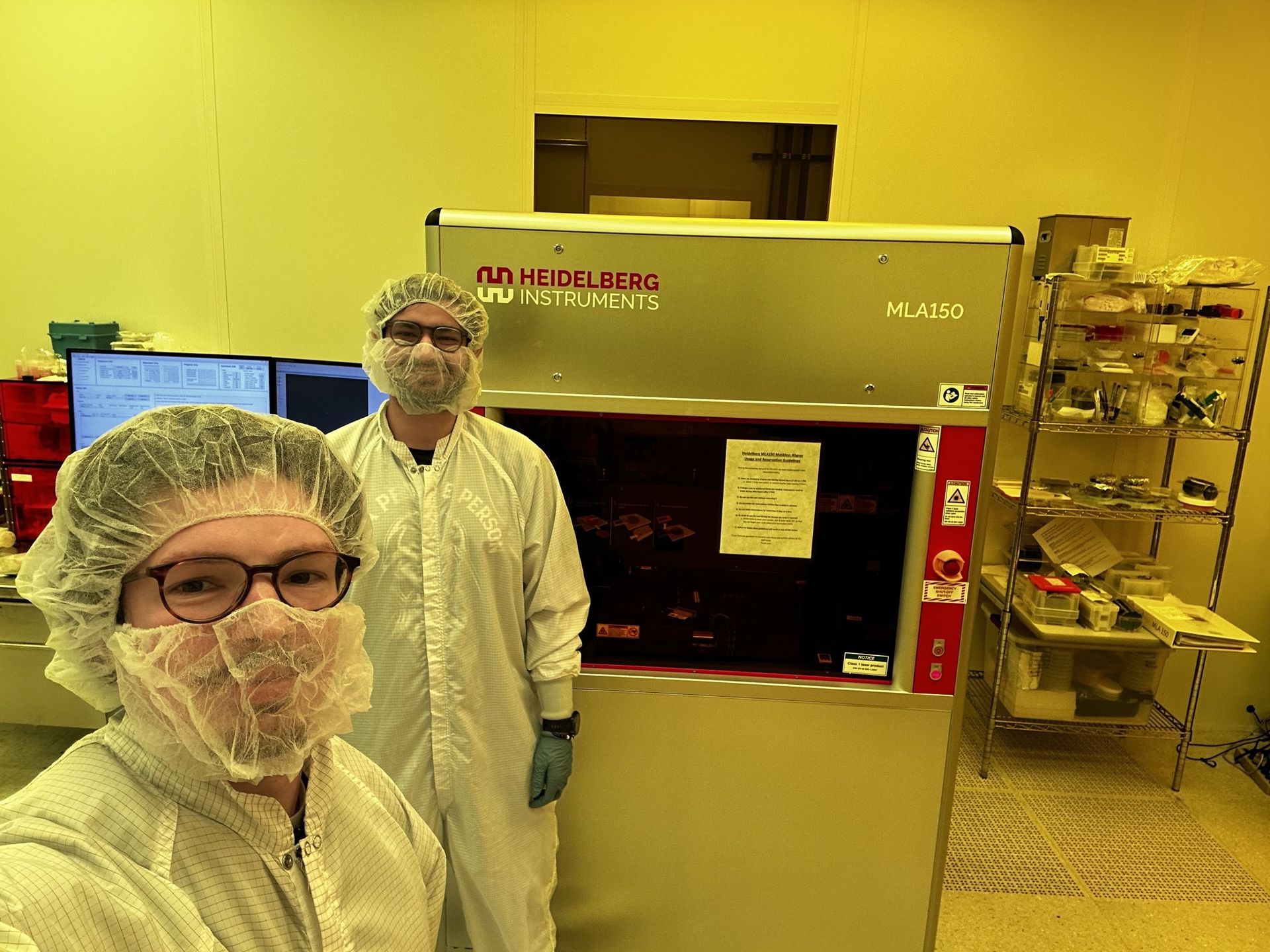 Jake Heisler and TJ in cleanroom garments at a Heidelberg Instruments MLA150 maskless aligner at the University of Maryland
