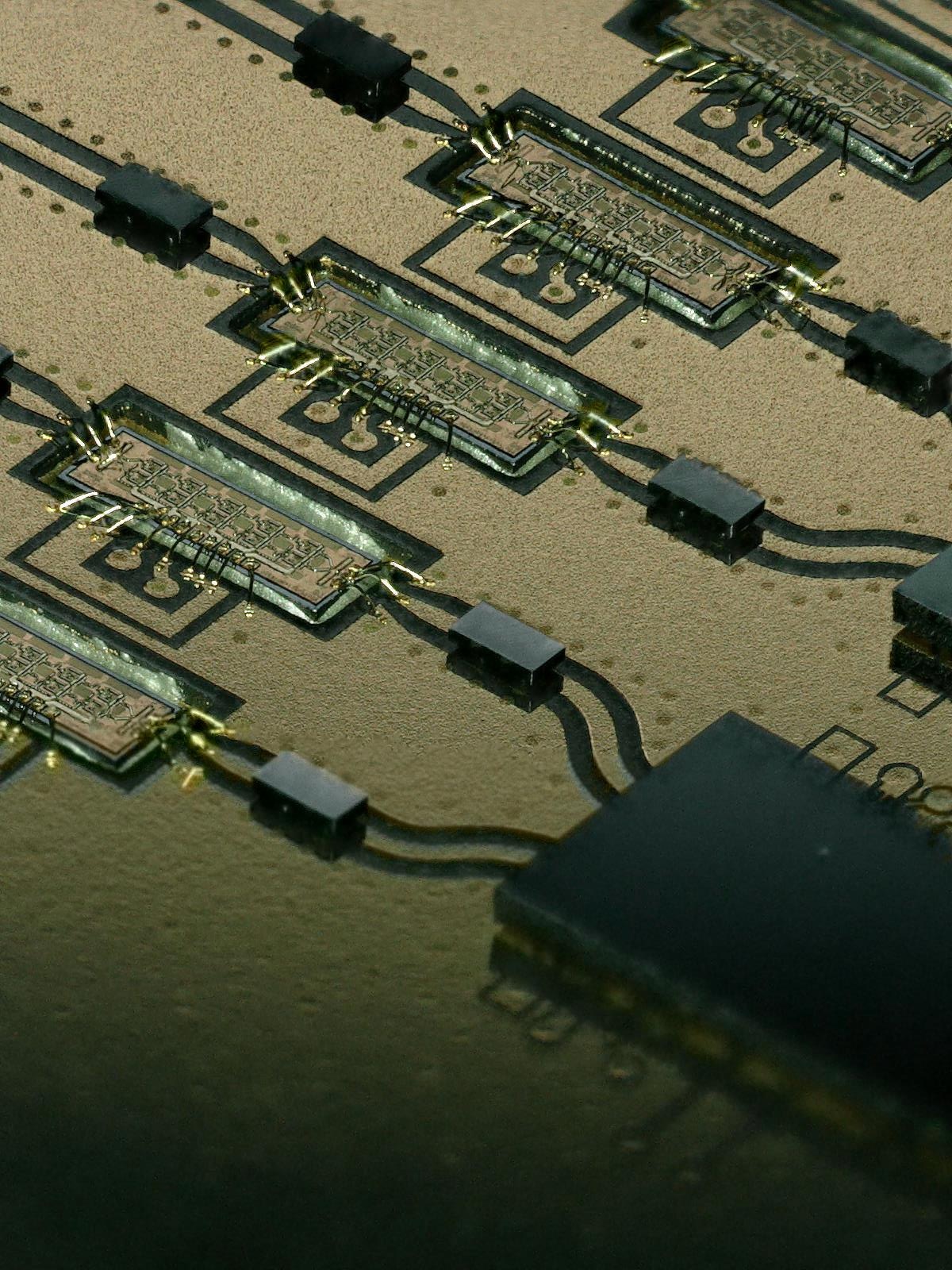 Macro photograph of CMOS and InP die wire bonded on a gold-plated multichip module with capacitors alongside